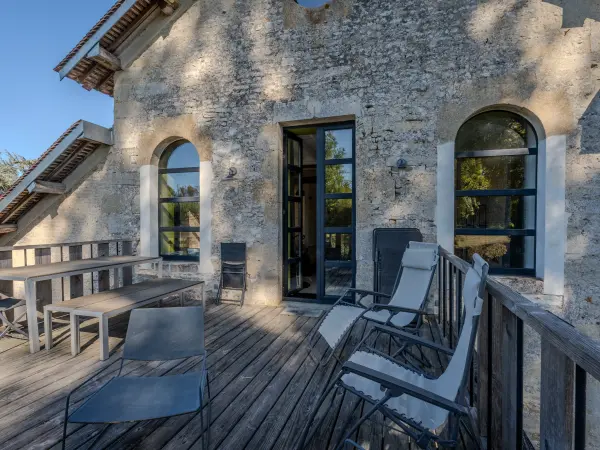 Façade en pierre avec terrasse en bois et fenêtres cintrées.