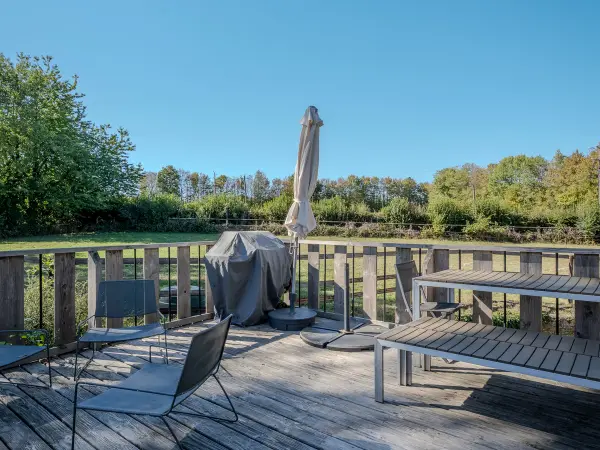 Terrasse en bois avec barbecue et parasol, vue sur un paddock.