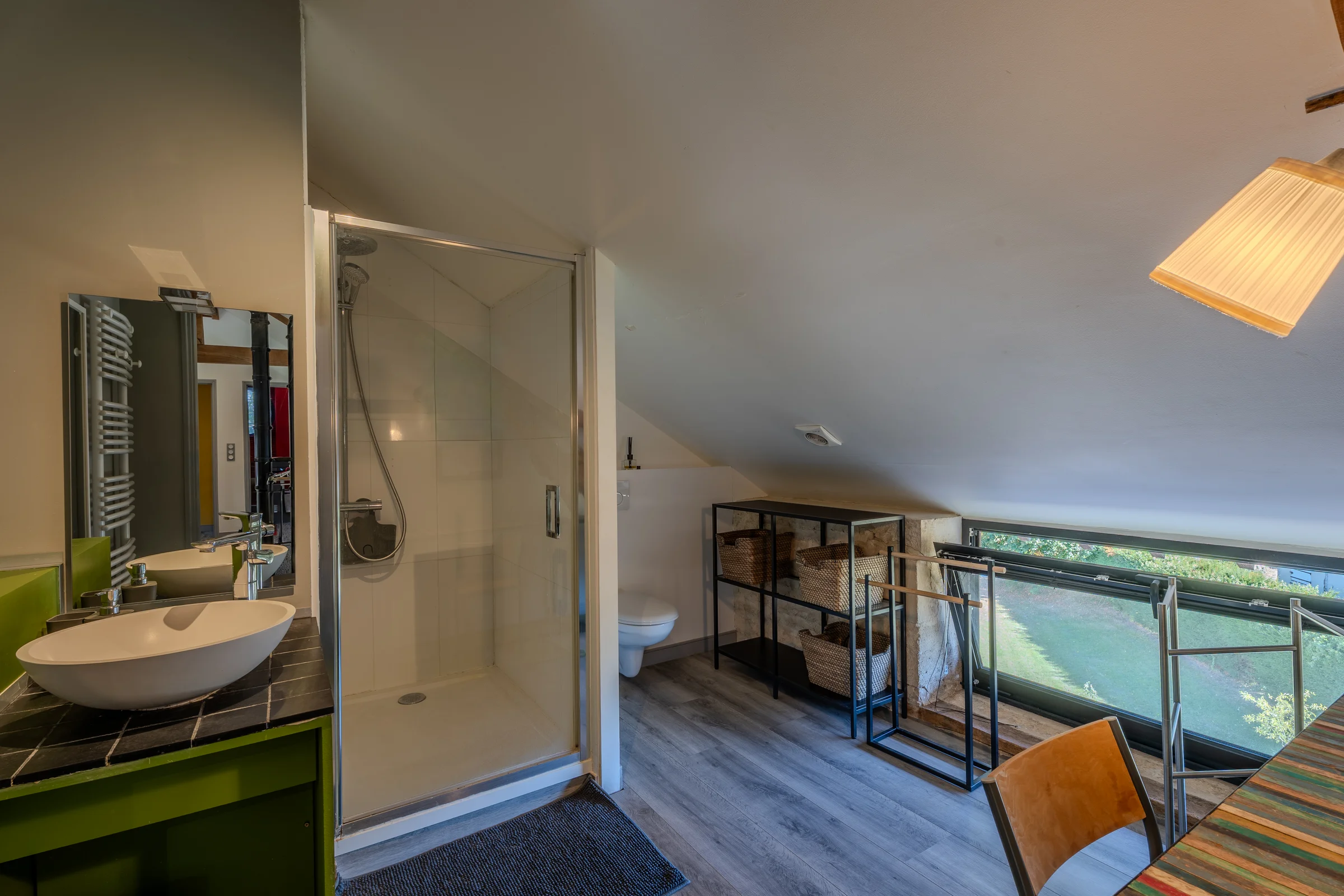 Salle de bains sous combles avec douche vitrée et vue sur l'extérieur.