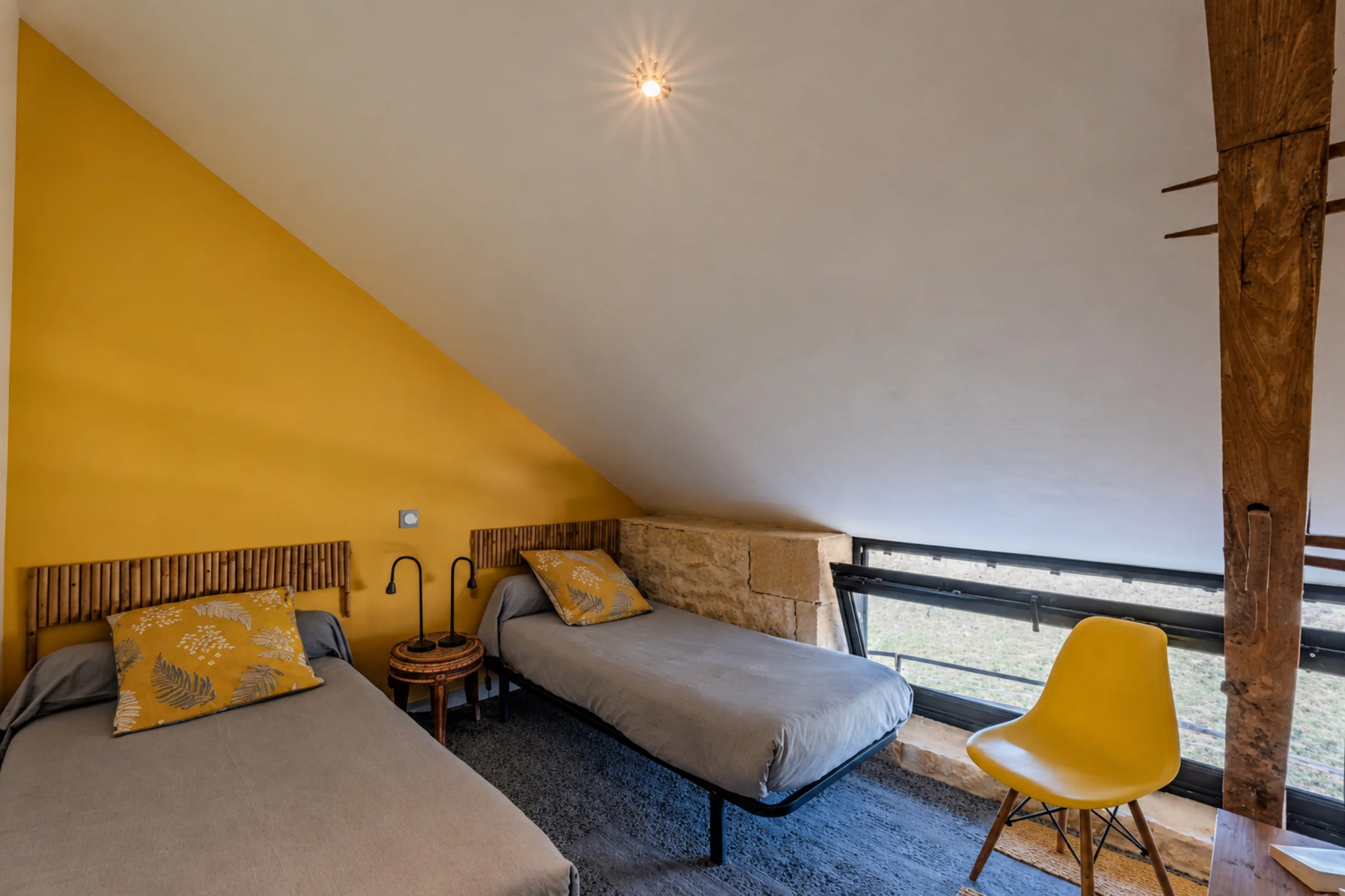 Chambre à deux lits sous combles, murs jaunes.