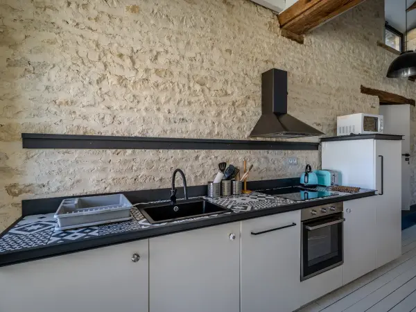 Plan de cuisine le long d'un mur en pierre, avec hotte et four intégré.