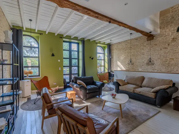 Salon avec poutres apparentes, mur en pierre et mur vert, mobilier en cuir et bois.