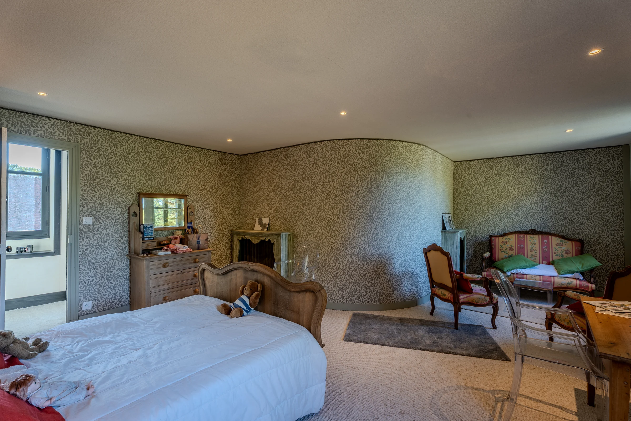 Chambre tapissée d'un motif végétal, avec cheminée et mobilier de style.