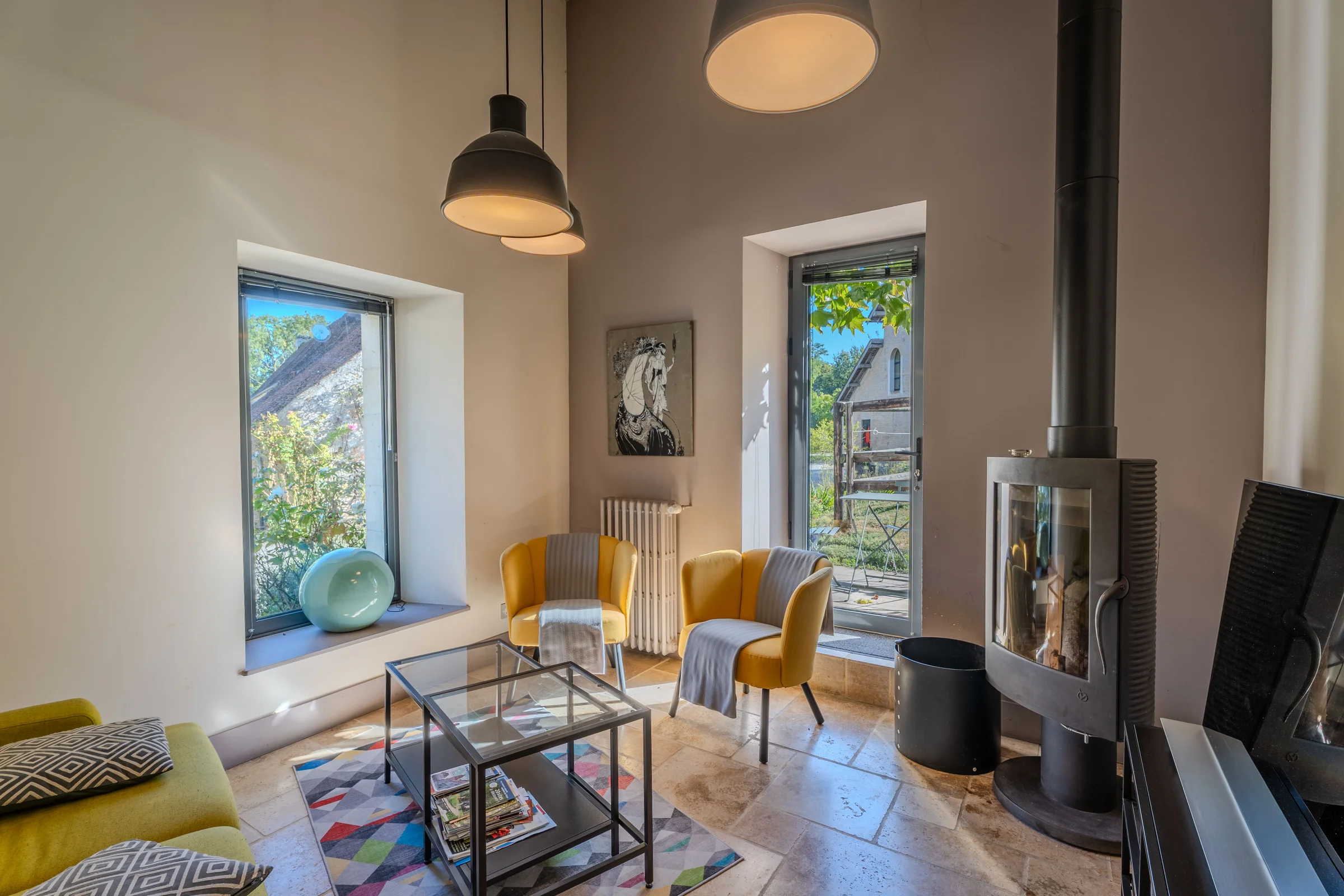 Salon avec poêle à bois et ouverture sur le jardin.