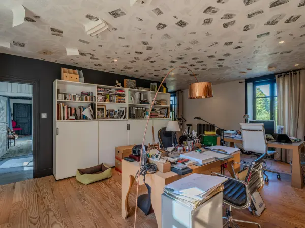 Vue d'ensemble du bureau avec rangements, bureaux et plafond habillé de pages imprimées.
