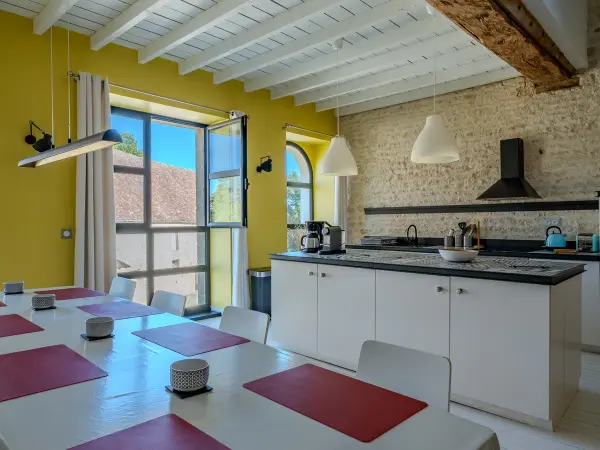 Cuisine ouverte sur la salle à manger, murs en pierre et plafond à poutres peintes.