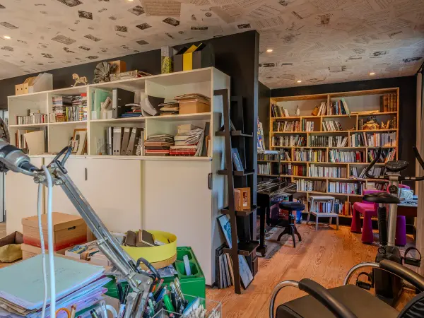 Bibliothèque et rangements dans le bureau, plafond habillé de pages imprimées.