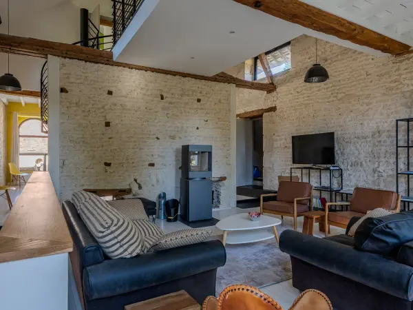 Salon sous charpente, mur en pierre et mezzanine en arrière-plan.