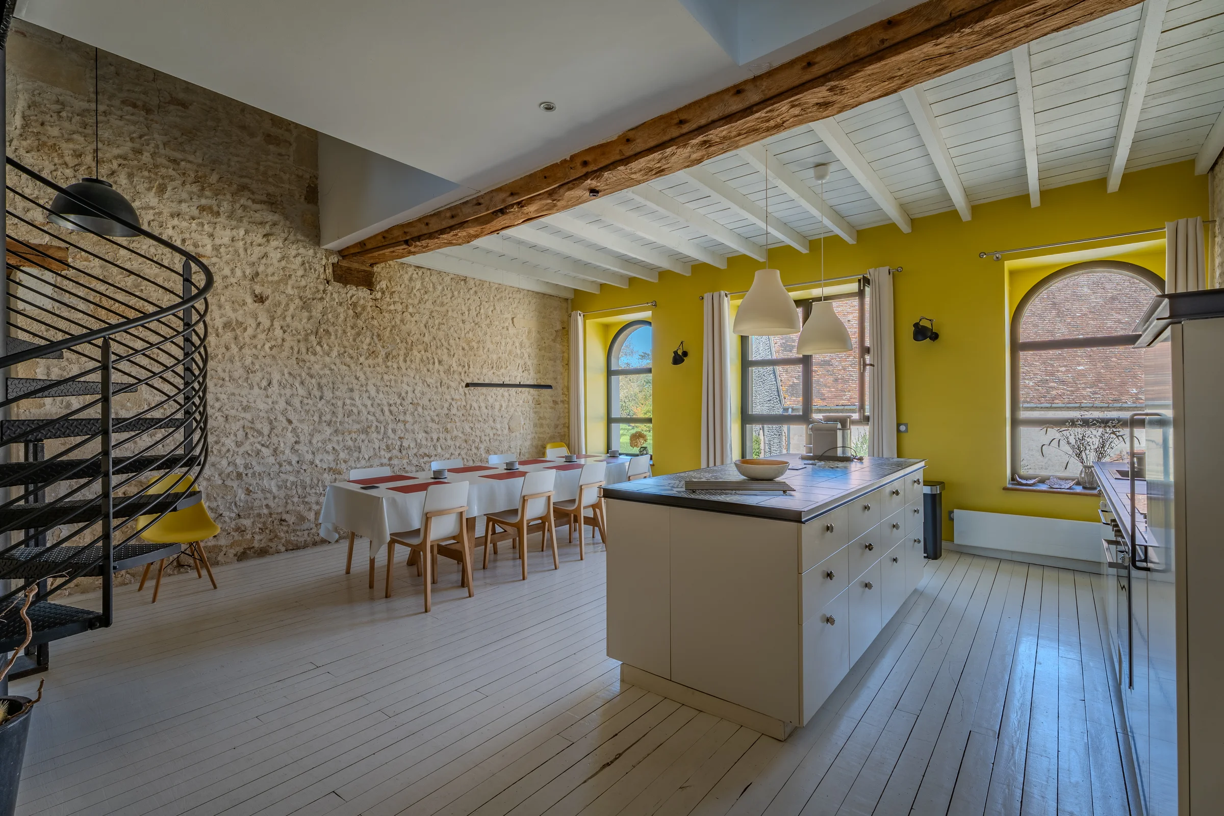 Salle à manger sous poutres, mur de pierre et escalier en colimaçon.