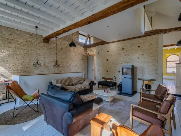 Salon sous charpente, poêle à bois et mezzanine en fond.
