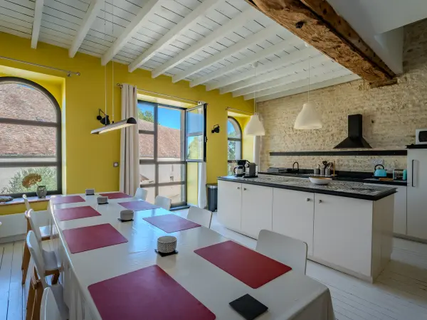 Cuisine ouverte sur salle à manger, murs jaunes et pierre apparente.