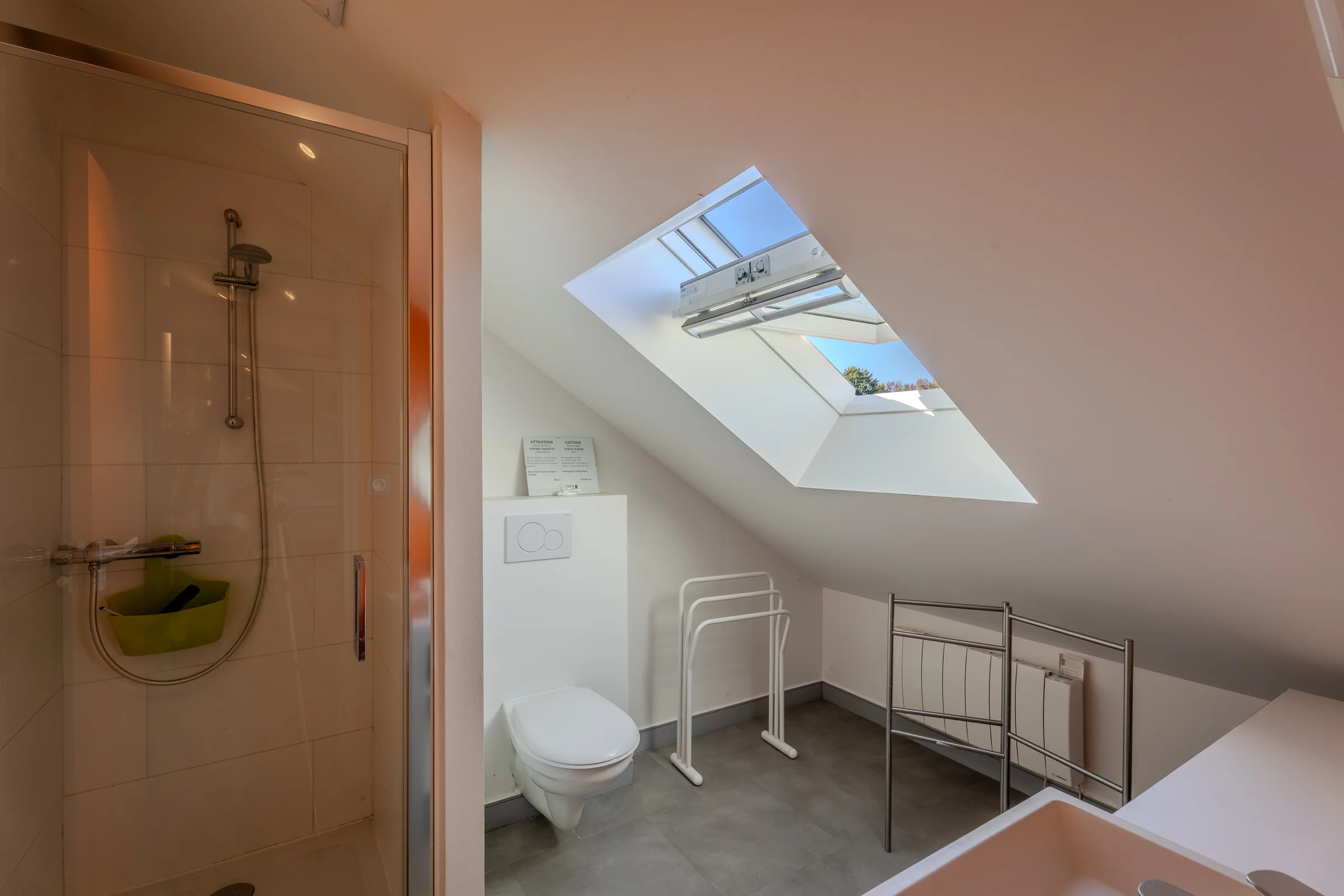 Salle de bains sous combles avec douche vitrée et large Velux.