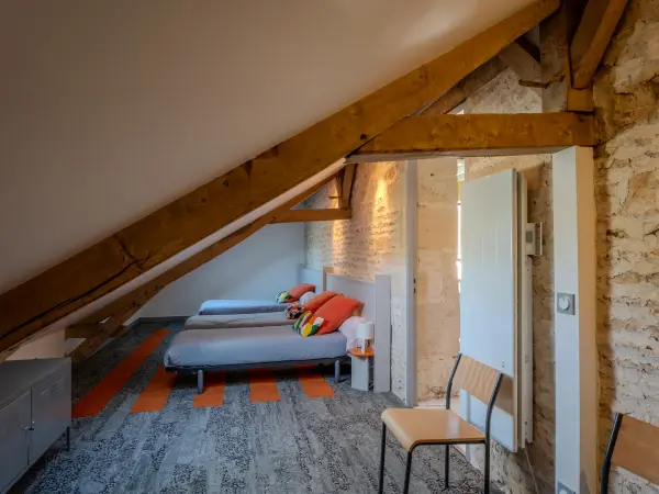 Chambre dortoir sous charpente apparente, avec mur en pierre.