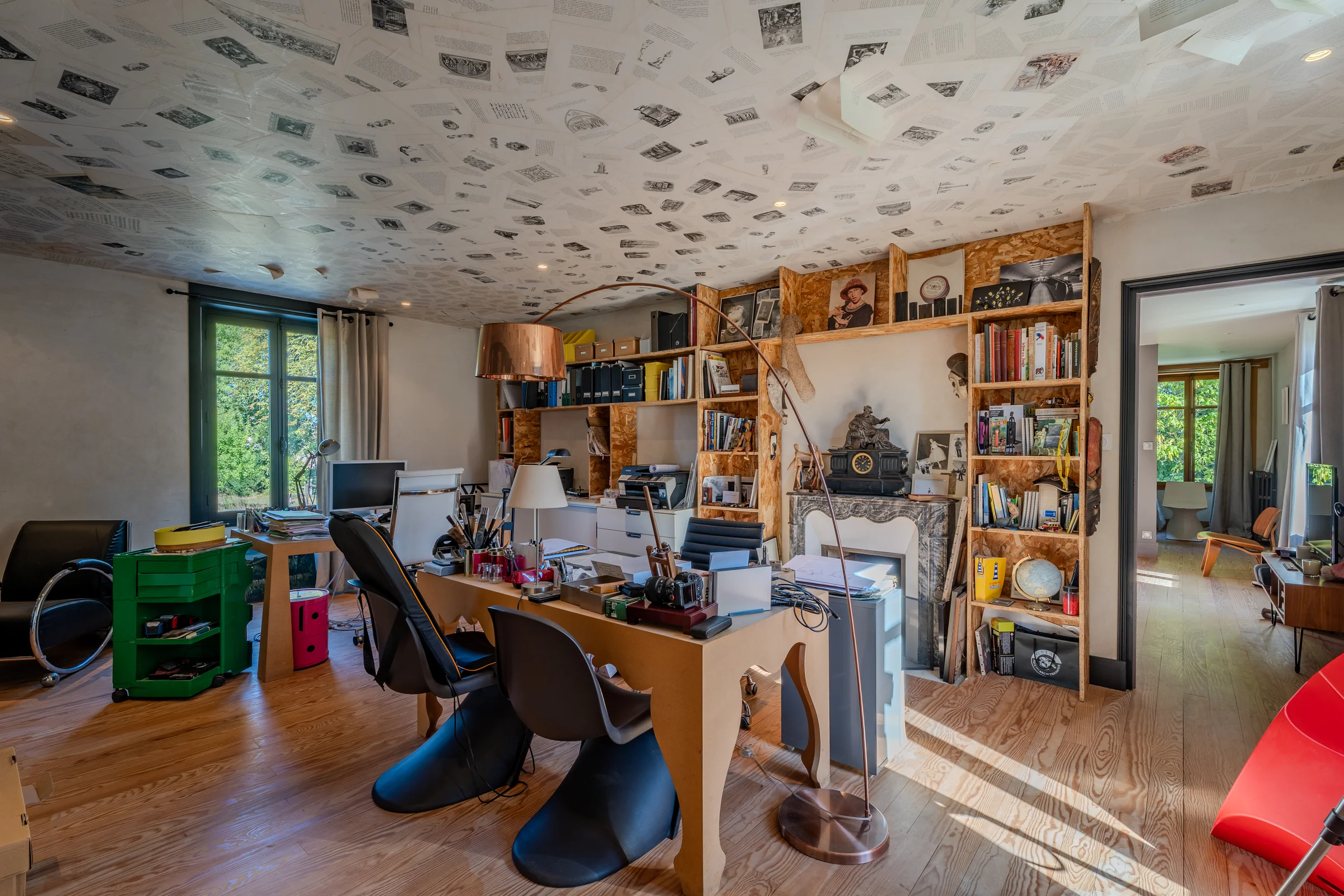Bureau au plafond habillé de pages imprimées, bibliothèque sur mesure et cheminée.