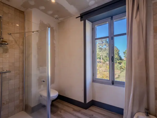 Salle de bains avec douche carrelée et vue sur jardin.