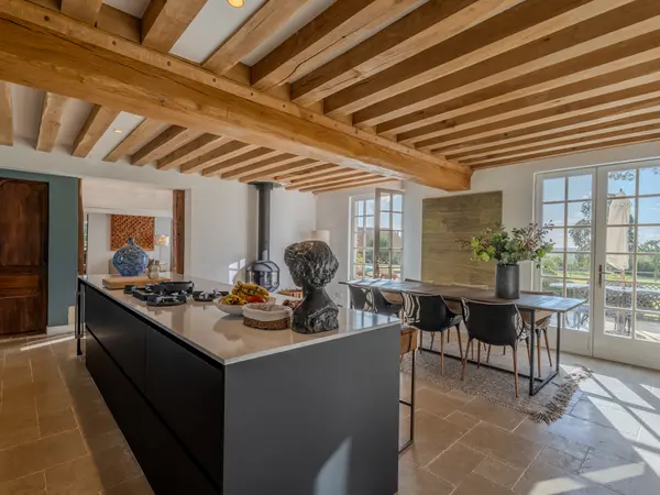 Cuisine ouverte sur la salle à manger, poêle à bois et poutres apparentes.