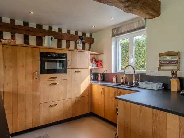 Cuisine aux poutres apparentes, meubles de bois clair et plan de travail sombre.