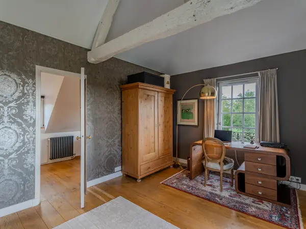 Chambre sous charpente avec armoire ancienne et coin bureau.