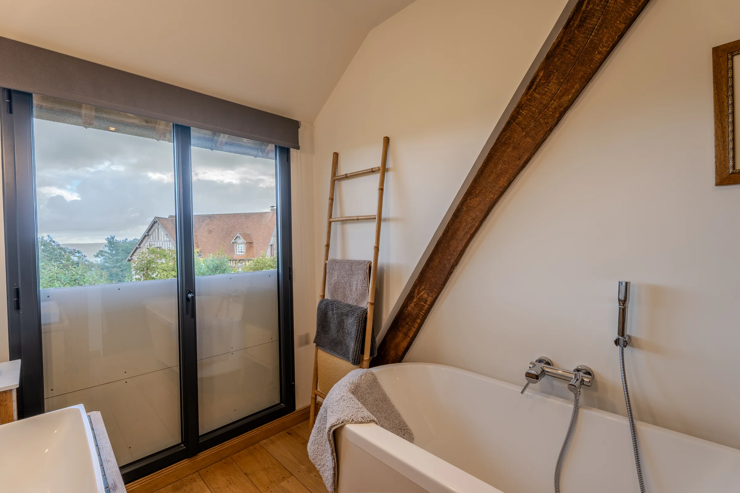Salle de bains mansardée, baignoire et baie vitrée sur la campagne.