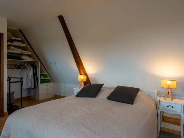 Chambre mansardée, poutre apparente et rangement sous pente.