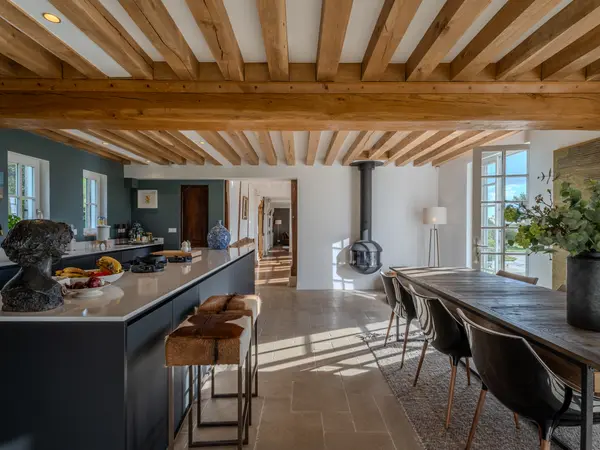Cuisine en enfilade avec poêle à bois et table de repas sous charpente apparente.