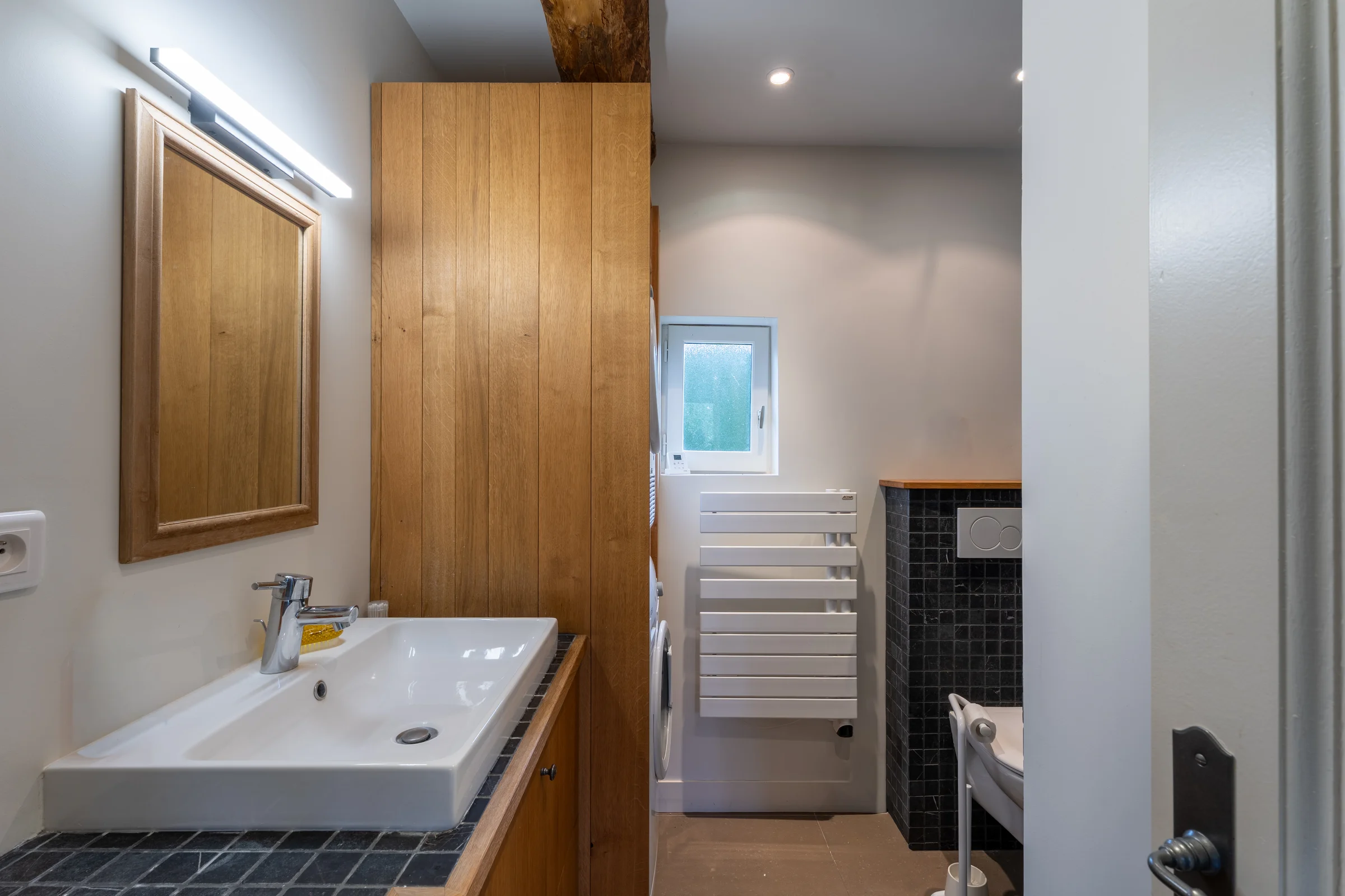 Salle de douche avec meuble bois et vue vers le WC.