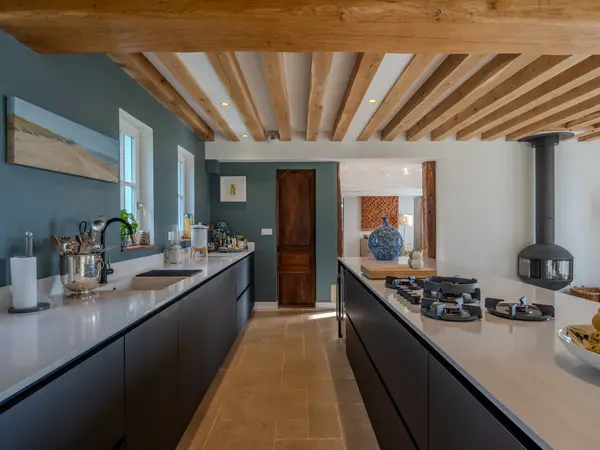 Cuisine traversante, plan de travail continu et poêle à bois en fond de pièce.