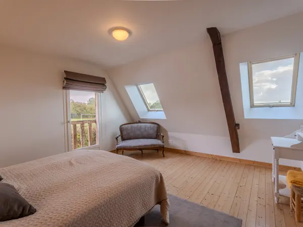 Chambre mansardée, parquet clair et accès balcon.