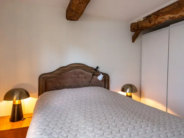Chambre, tête de lit entre poutre apparente et placard intégré.