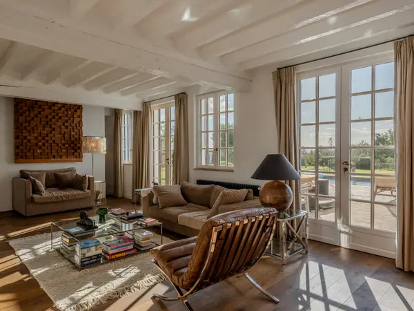 Salon aux poutres blanches avec vue directe sur la piscine depuis les baies vitrées.