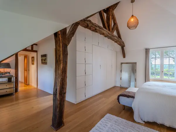 Chambre sous charpente, poutres apparentes et vue sur le jardin.