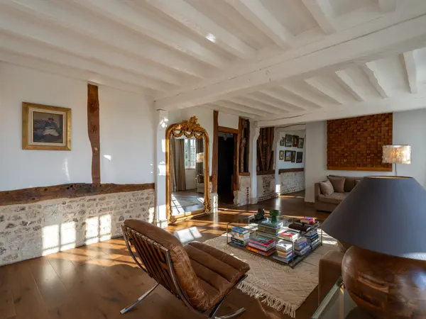 Angle du salon révélant un mur en pierre apparente et une ouverture vers les pièces voisines.