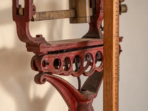 Détail d'un ancien mécanisme en fonte peinte et règle graduée en bois.