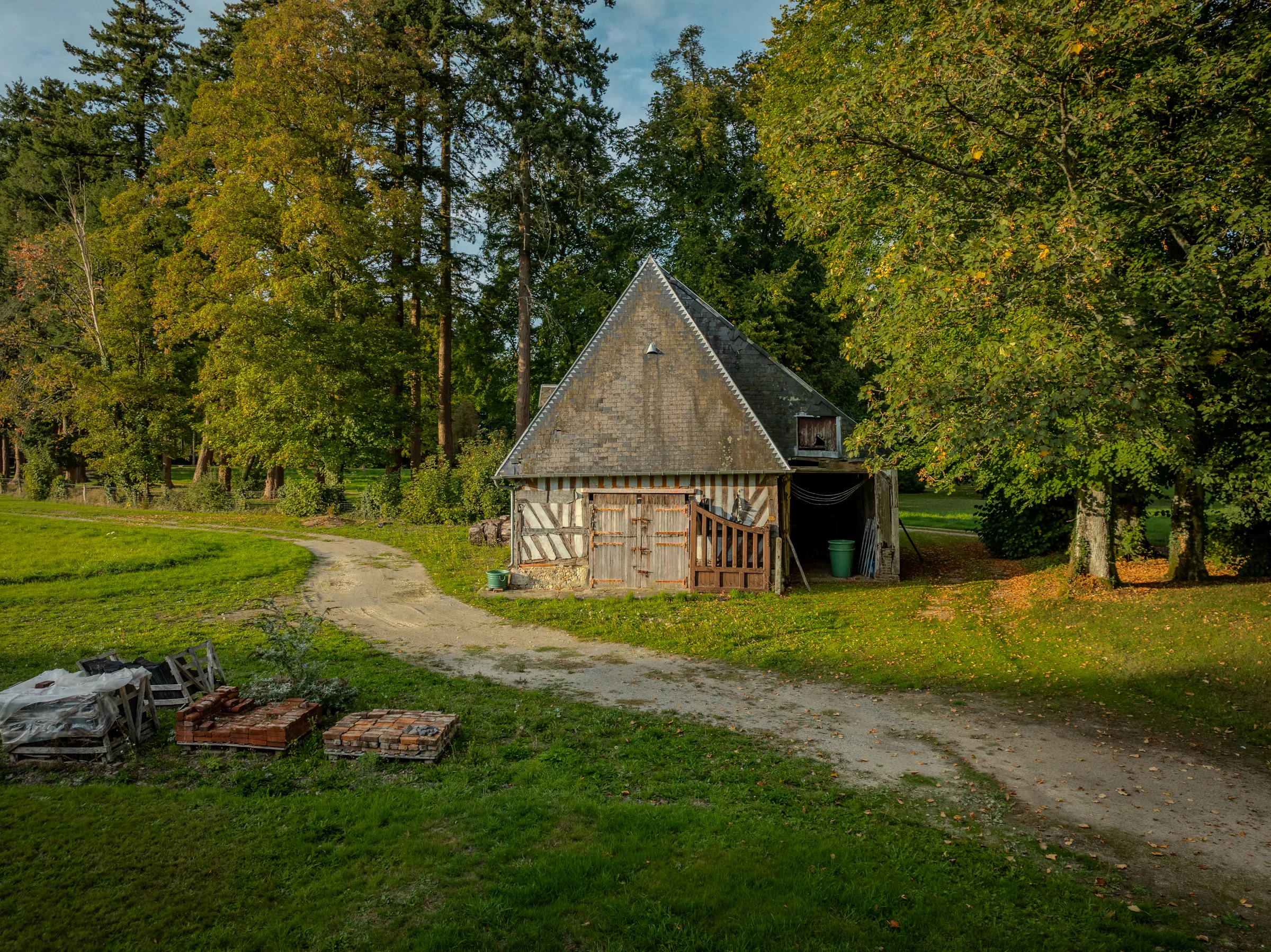 Écuries en pans de bois à toiture pentue, en bordure d'allée, dans le parc.
