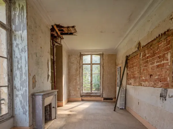 Chambre avec cheminée en marbre d'aspect, mur dégarni laissant voir la maçonnerie en brique.