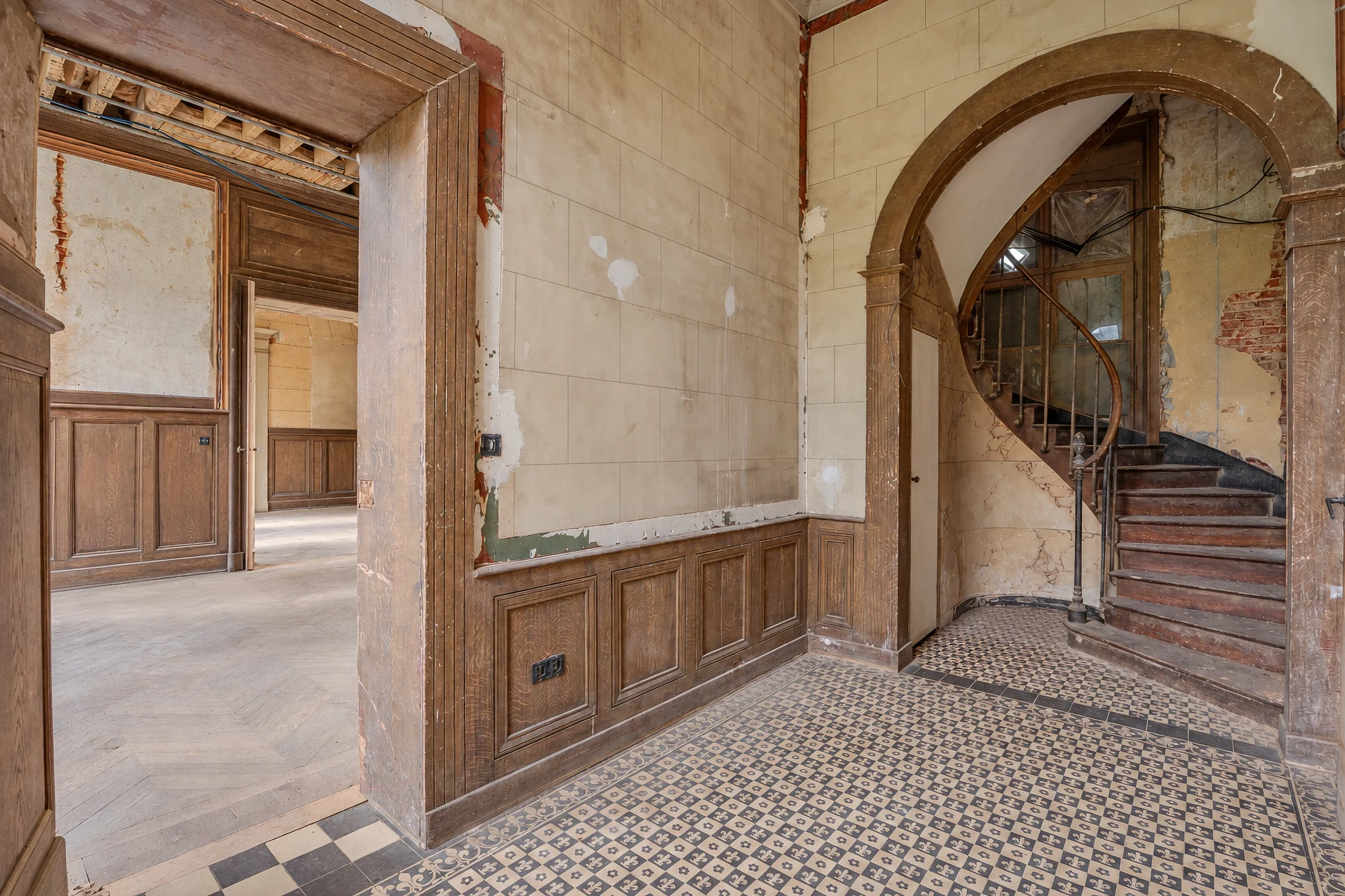 Vestibule en travaux, arche vers l'escalier à vis et sol en carreaux de ciment anciens.