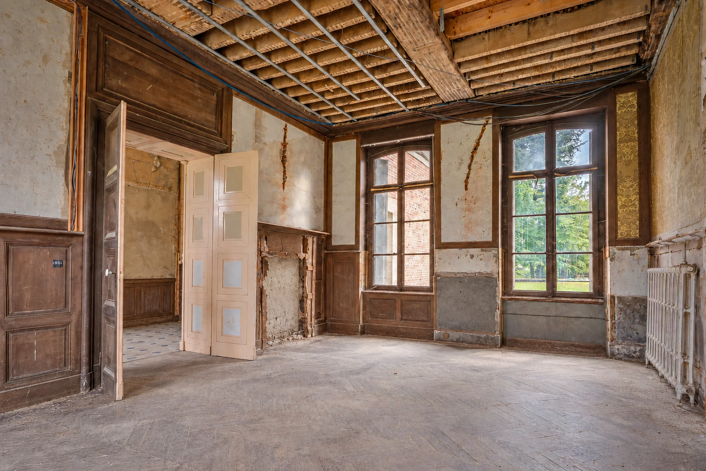 Salle à manger en cours de restauration, charpente apparente et cheminée dépouillée.