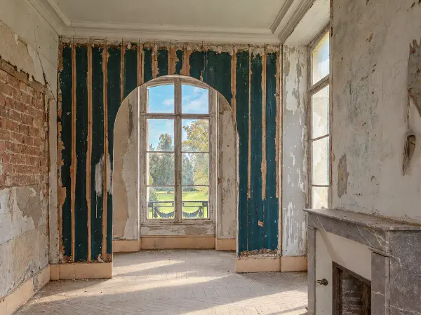 Chambre ouvrant par une baie cintrée sur un balcon et le parc, boiseries en cours de restauration.