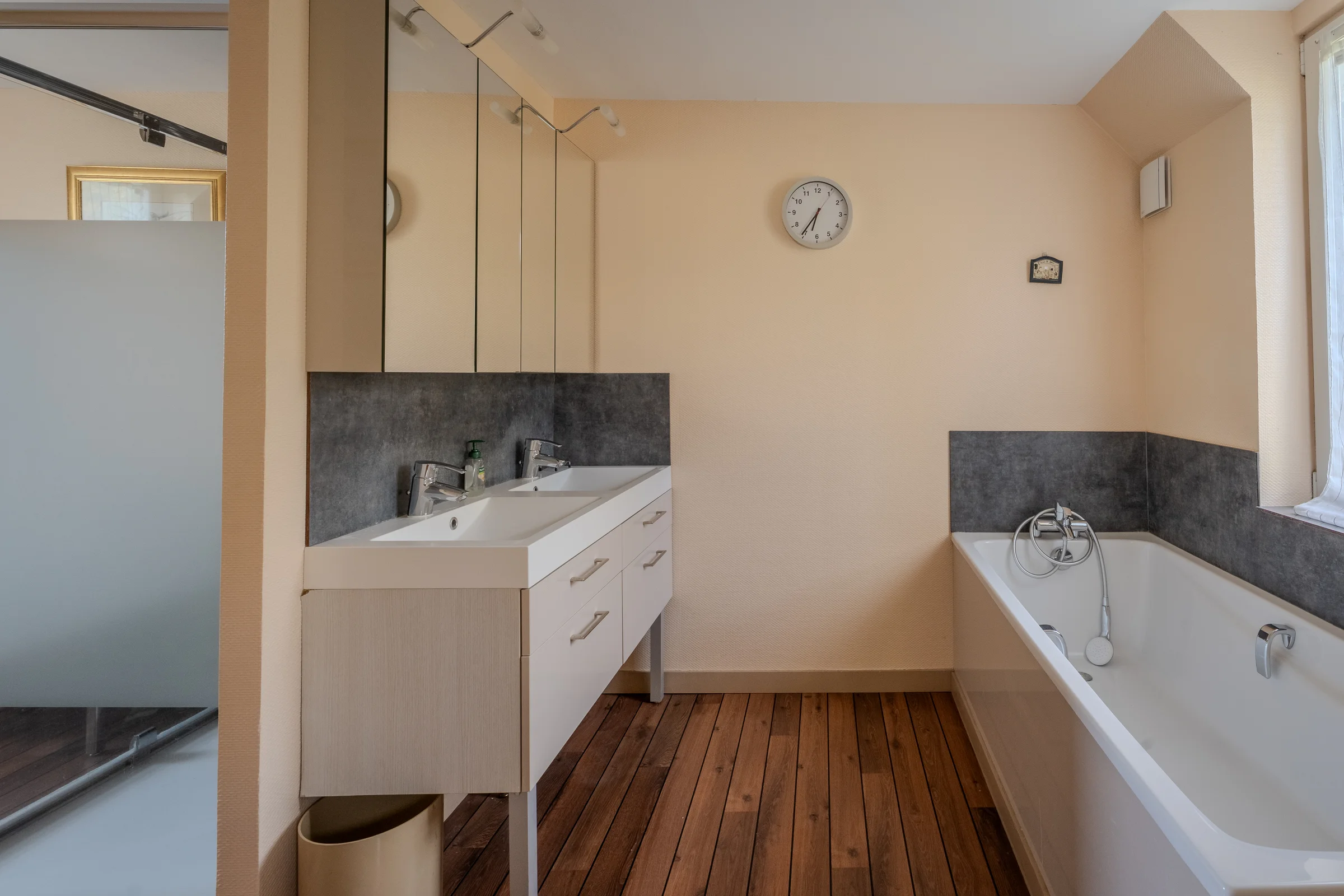 Salle de bains avec double vasque et baignoire, sol en lames de bois.