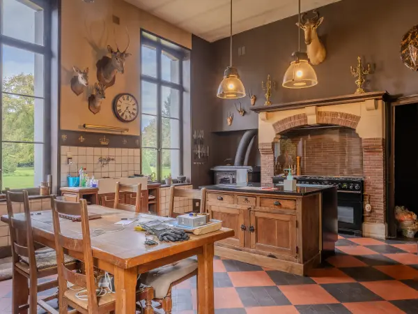Cuisine aux volumes hauts, sol à damier et cheminée en brique abritant le fourneau.