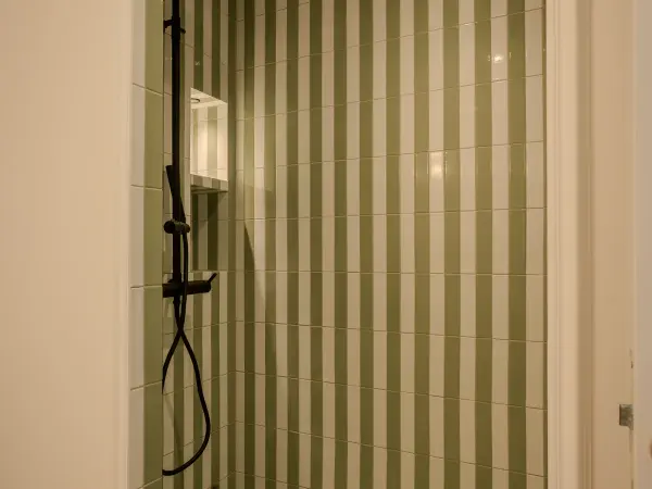 Douche carrelée à rayures vertes, robinetterie noire.