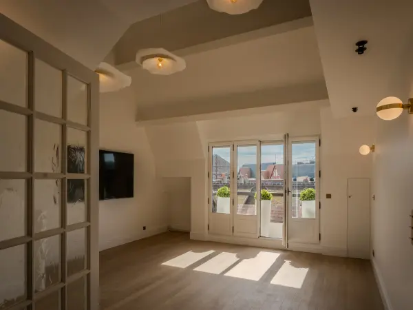 Salon du 1er niveau sous combles, éclairé par une porte fenêtre ouvrant sur balcon filant.