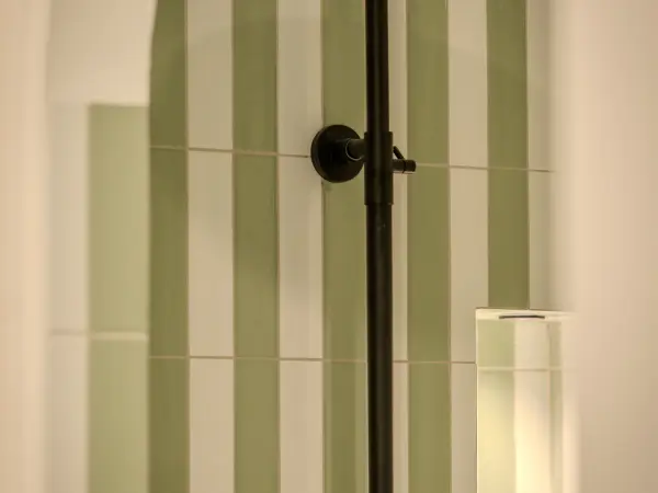 Détail de colonne de douche sur carrelage à lames vertes.